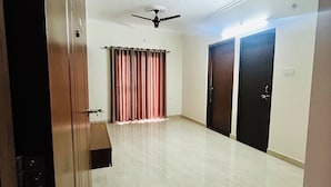 Um quarto amplo com piso lustroso, duas portas, um ventilador de teto e uma janela com cortinas.