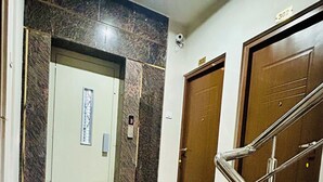 Um corredor com piso de mármore, porta de madeira e escada de metal.