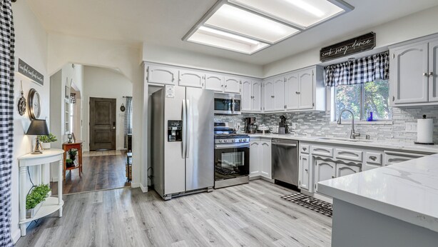 A modern kitchen with white cabinetry, a stainless steel refrigerator, an oven, and a microwave. There is a window with a view of greenery outside. - Pet-friendly Yard! Home 3 Mi to Sky River Casino (Elk Grove)