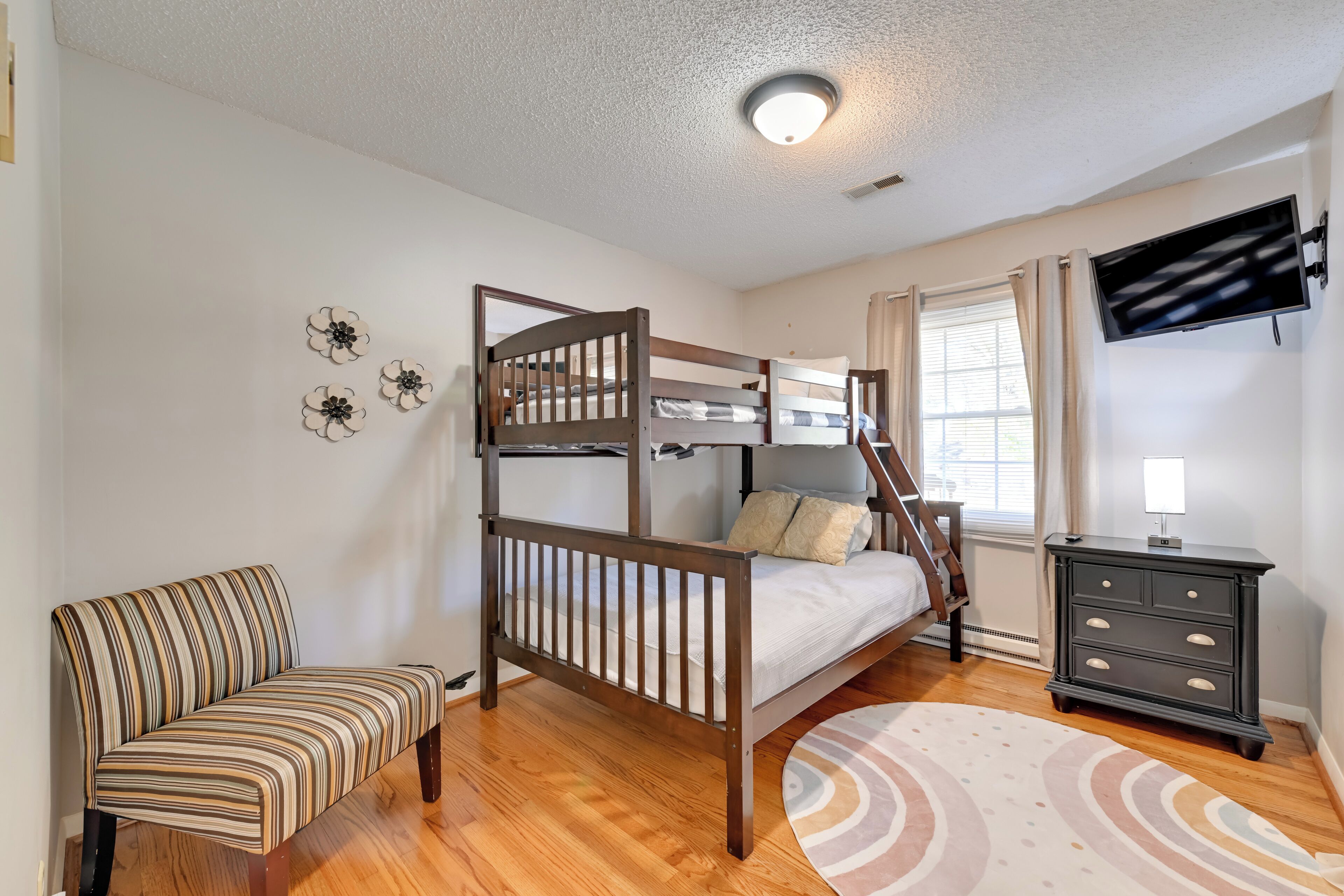 A bedroom with a bunk bed, a striped chair, a dresser, and a TV.