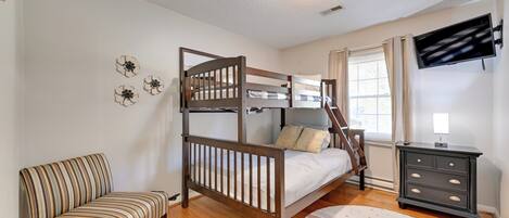A bedroom with a bunk bed, a striped chair, a dresser, and a TV.