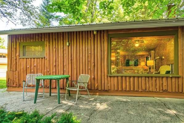 A wooden cabin with a small porch, a table, two chairs, and a window. - Cozy 'rivershire Retreat Cabin' Near Traverse City (Traverse City)