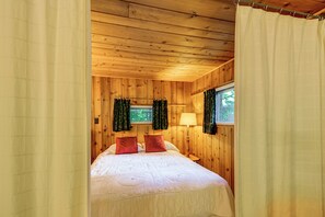 A wooden cabin bedroom with a bed, curtains, and a window. - Cozy 'rivershire Retreat Cabin' Near Traverse City (Traverse City)