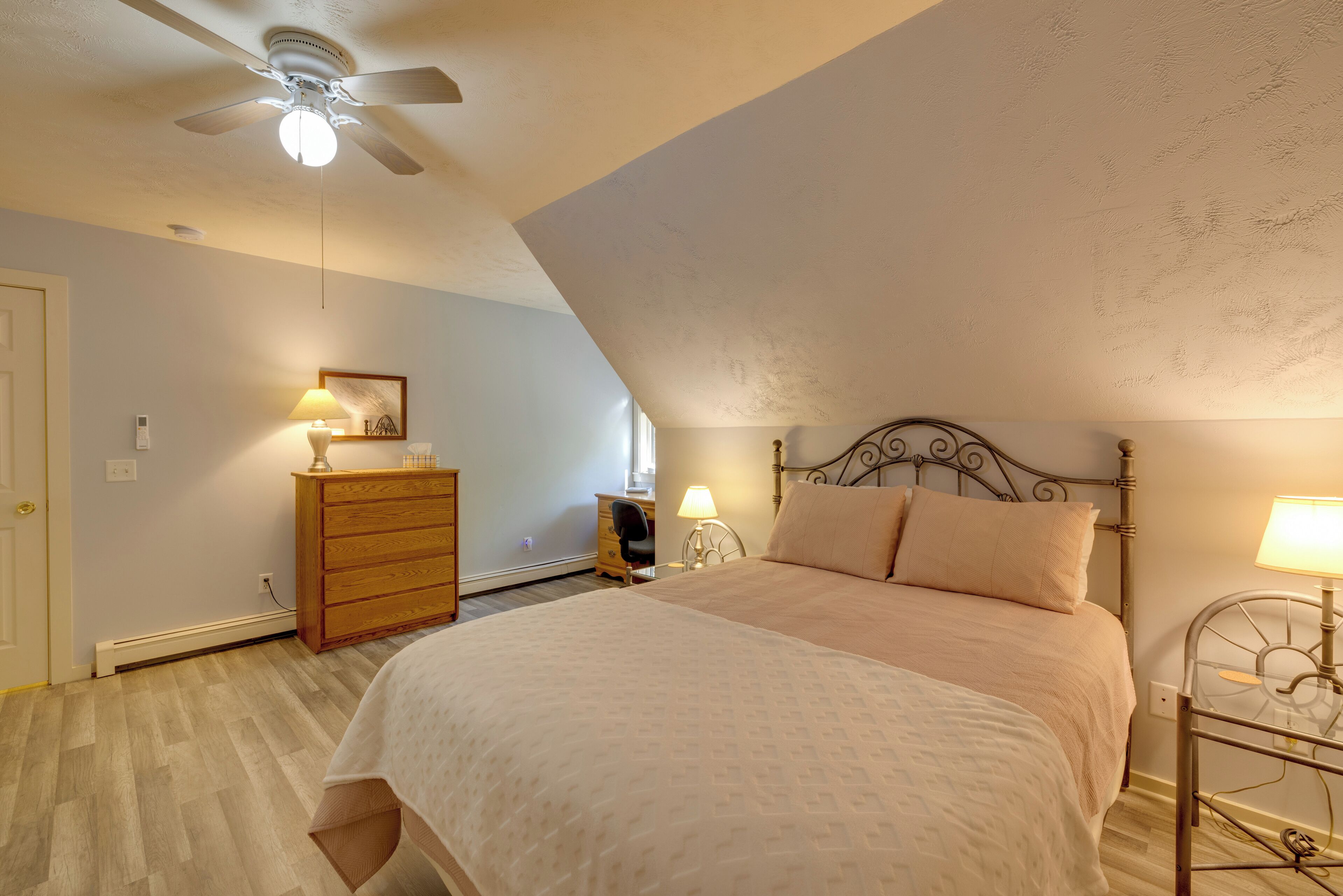 Une chambre à coucher comprenant un lit, une commode, un bureau, une chaise et un ventilateur de plafond.