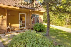 A yellow house with a porch, a chair, and a small garden. - Riverside Serenity - Rivershire Retreat Guesthouse (Traverse City)
