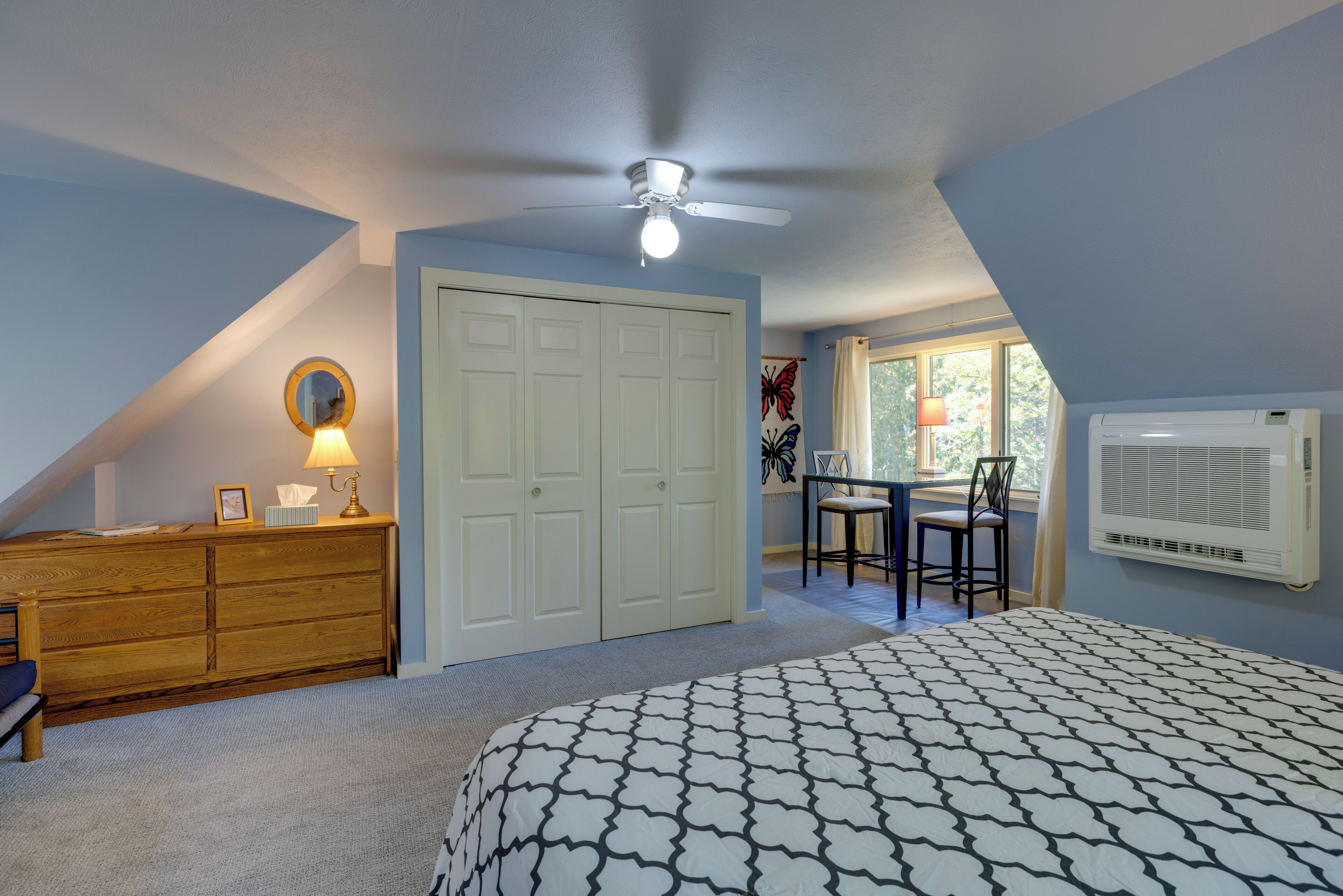 A bedroom with a bed, a dresser, a desk, a chair, a ceiling fan, and a window.