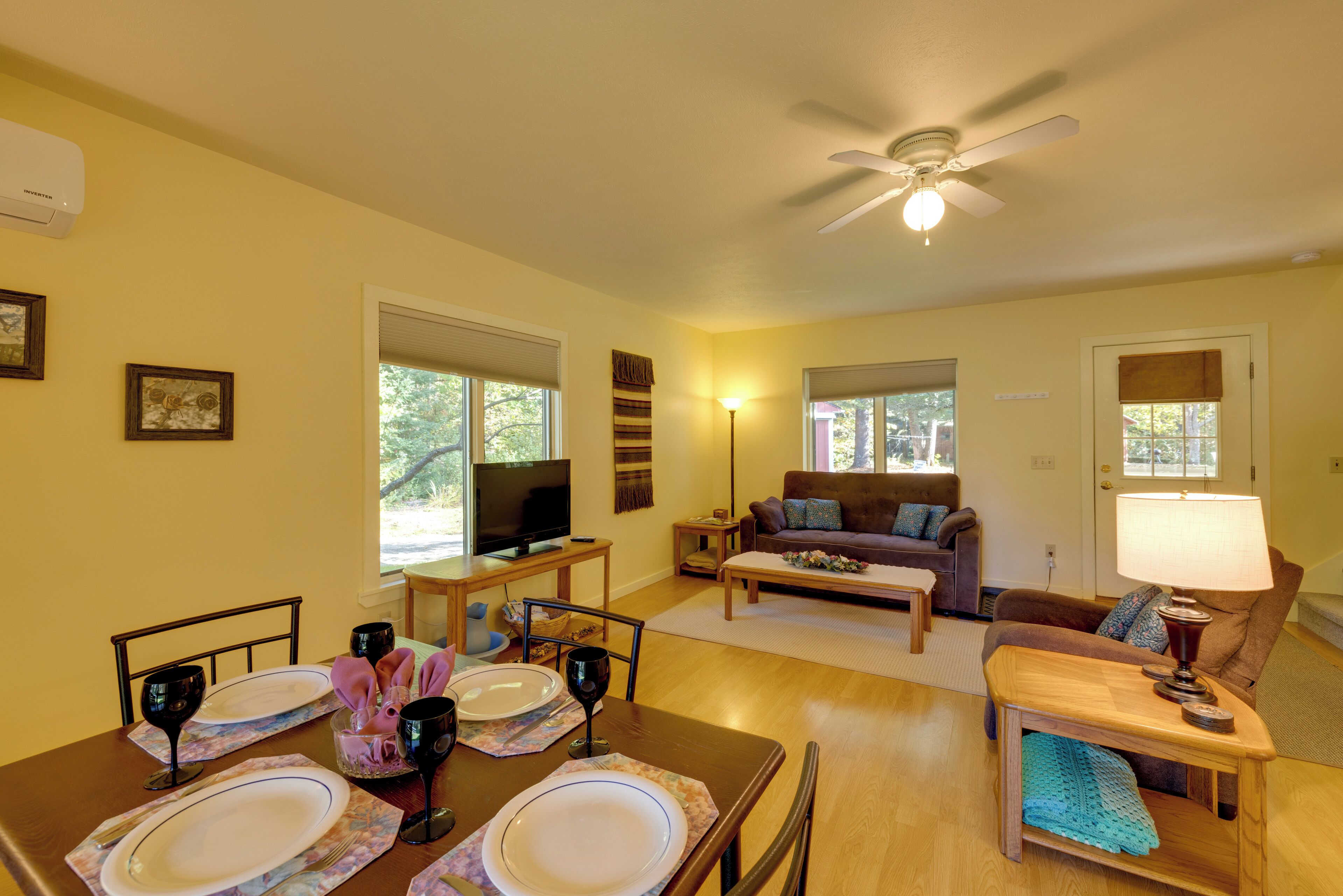 A dining area with a table set for four, a television, a sofa, and a ceiling fan.