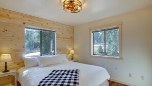 A bedroom with a wooden wall, two windows, a bed with white bedding, a checkered throw blanket, and two bedside lamps. - High Noon Hideaway: Zion Cabin w/ Fire Pit! (Duck Creek Village)