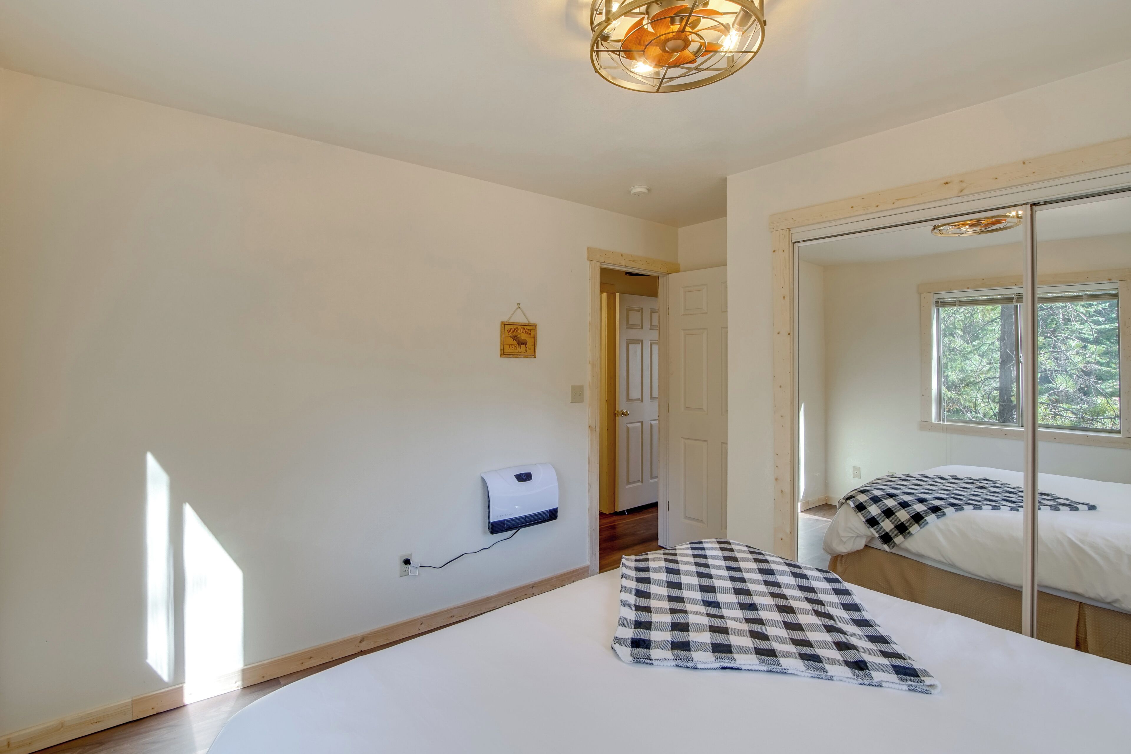 A bedroom with a bed, a checkered pillow, a wall-mounted air purifier, and a window with a view of trees.