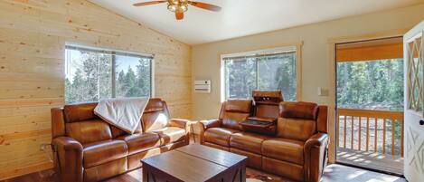 A log cabin interior with leather sofas, a wooden coffee table, and a ceiling fan.