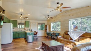 A spacious living area with a leather sofa, a wooden coffee table, and a dining table with chairs. A kitchen with green cabinets and a central island is visible in the background. - High Noon Hideaway: Zion Cabin w/ Fire Pit! (Duck Creek Village)