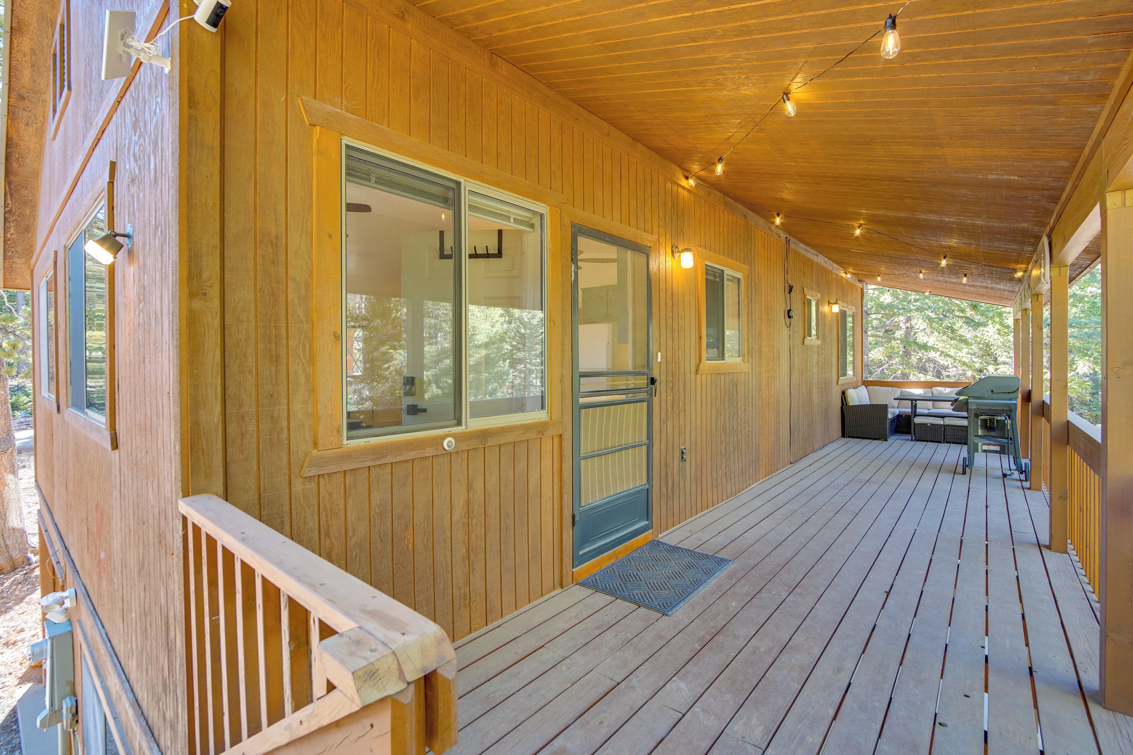A wooden deck with a covered area, large windows, and outdoor furniture.