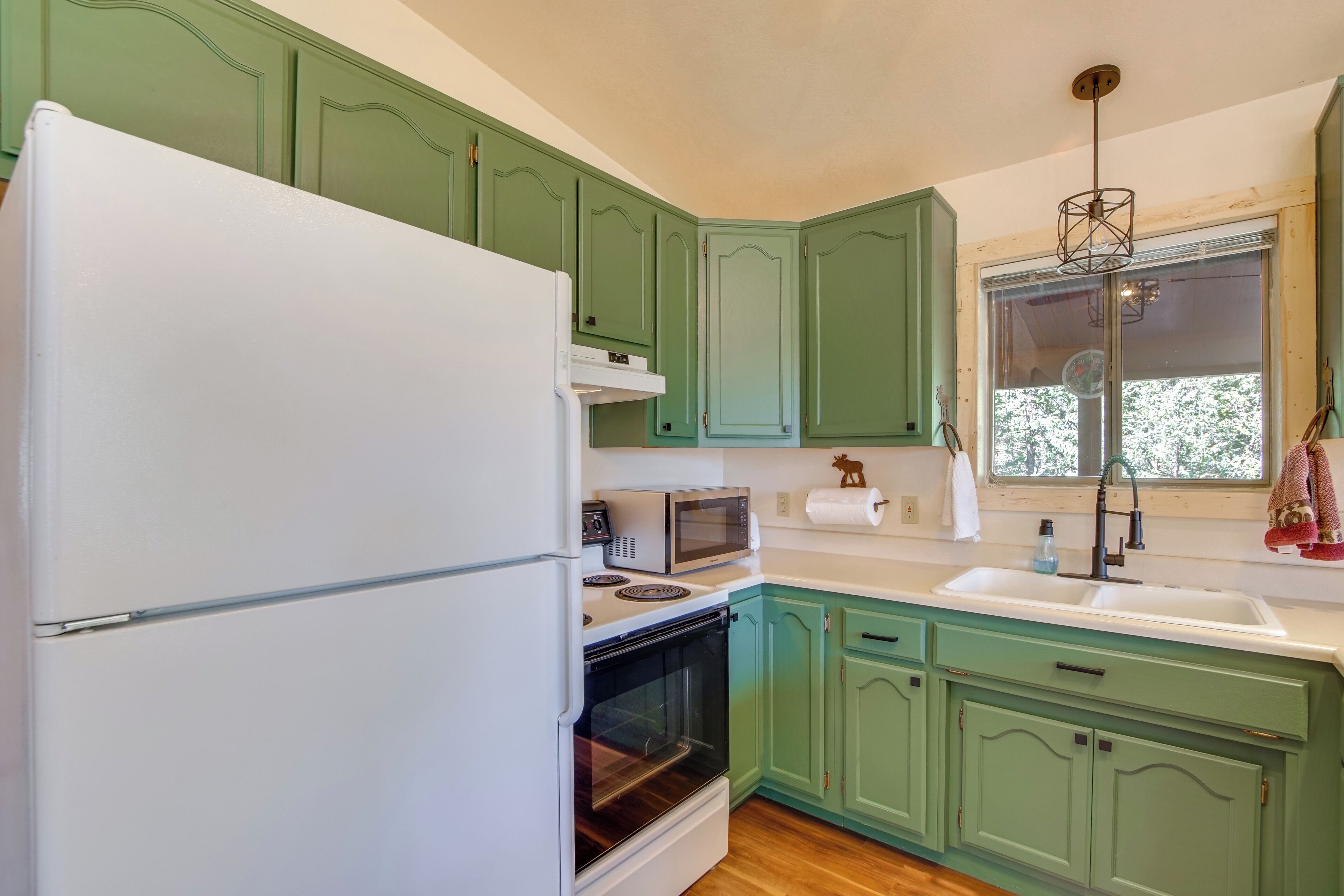 A kitchen with green cabinets, a white refrigerator, a microwave, and a sink.