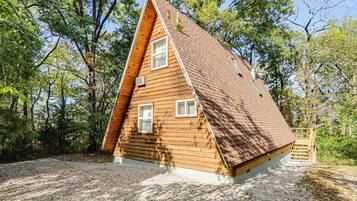 A wooden cabin with a sloped roof, surrounded by trees.