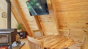 Un interior de cabaña acogedor con una estufa de leña, una mesa redonda de madera y cuatro sillas de madera.
