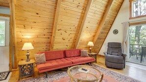 Un dormitorio estilo loft acogedor, con techo inclinado de madera, un sofá rojo, una mesita de centro de vidrio y un sillón reclinable gris.
