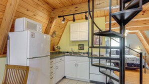 Una cocina con armarios blancos, un refrigerador blanco, una silla de madera y una escalera en espiral.