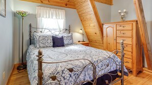 Un dormitorio con techo inclinado, una cama con colcha estampada, un aparador de madera y una lámpara de pie.