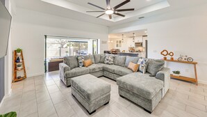 A spacious living room with a large sectional sofa, a ceiling fan, and a view into the kitchen.