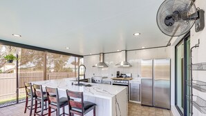 A modern kitchen with a large island, stainless steel appliances, and a fan.