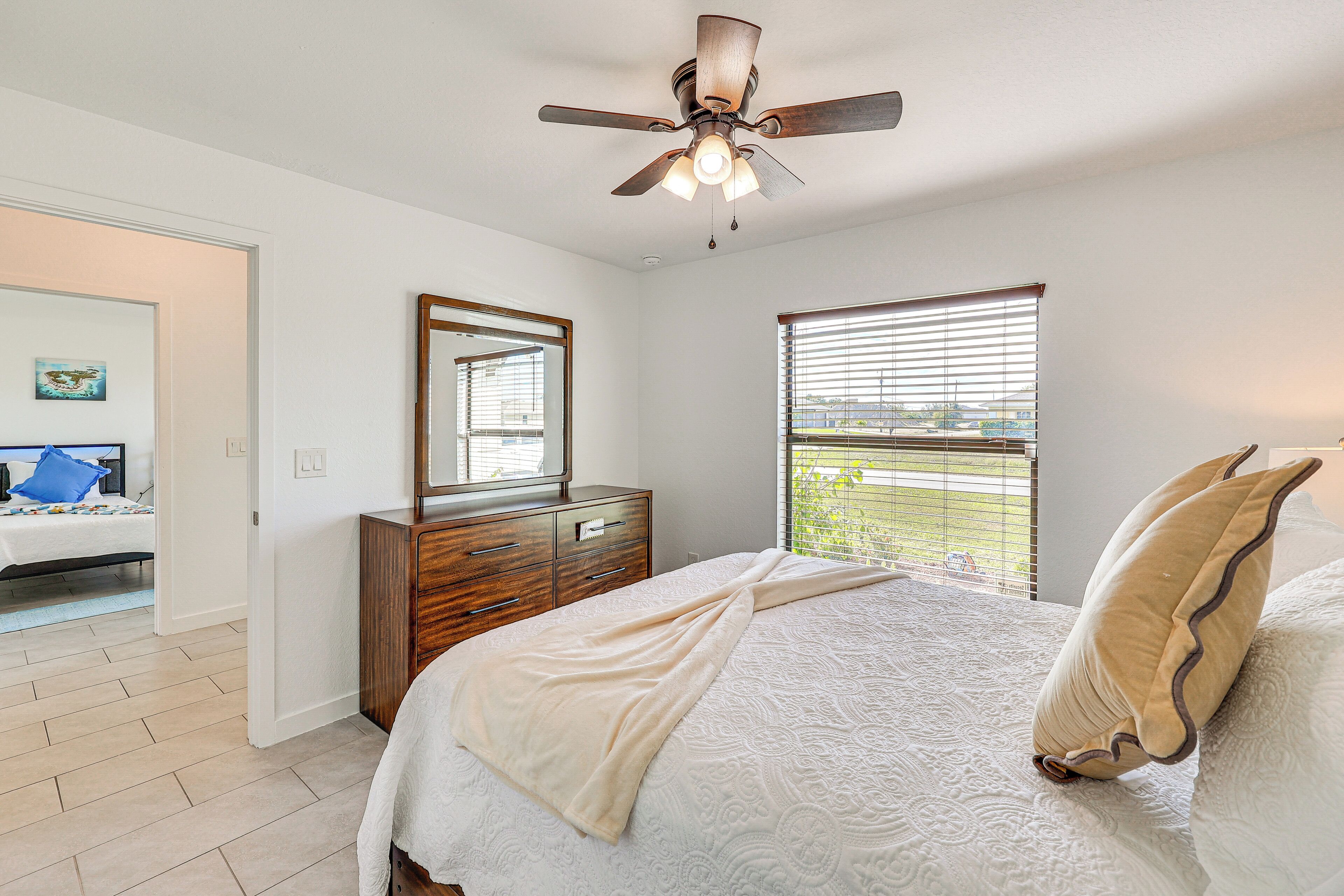 Un dormitorio con cama, ventilador de techo, cómoda, espejo y ventana con persianas.