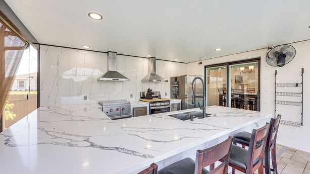 A kitchen with a large marble island, stainless steel appliances, and a fan on the wall.