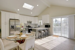 A modern kitchen with white cabinets, a stainless steel refrigerator, a built-in oven, and a large island with bar stools.
