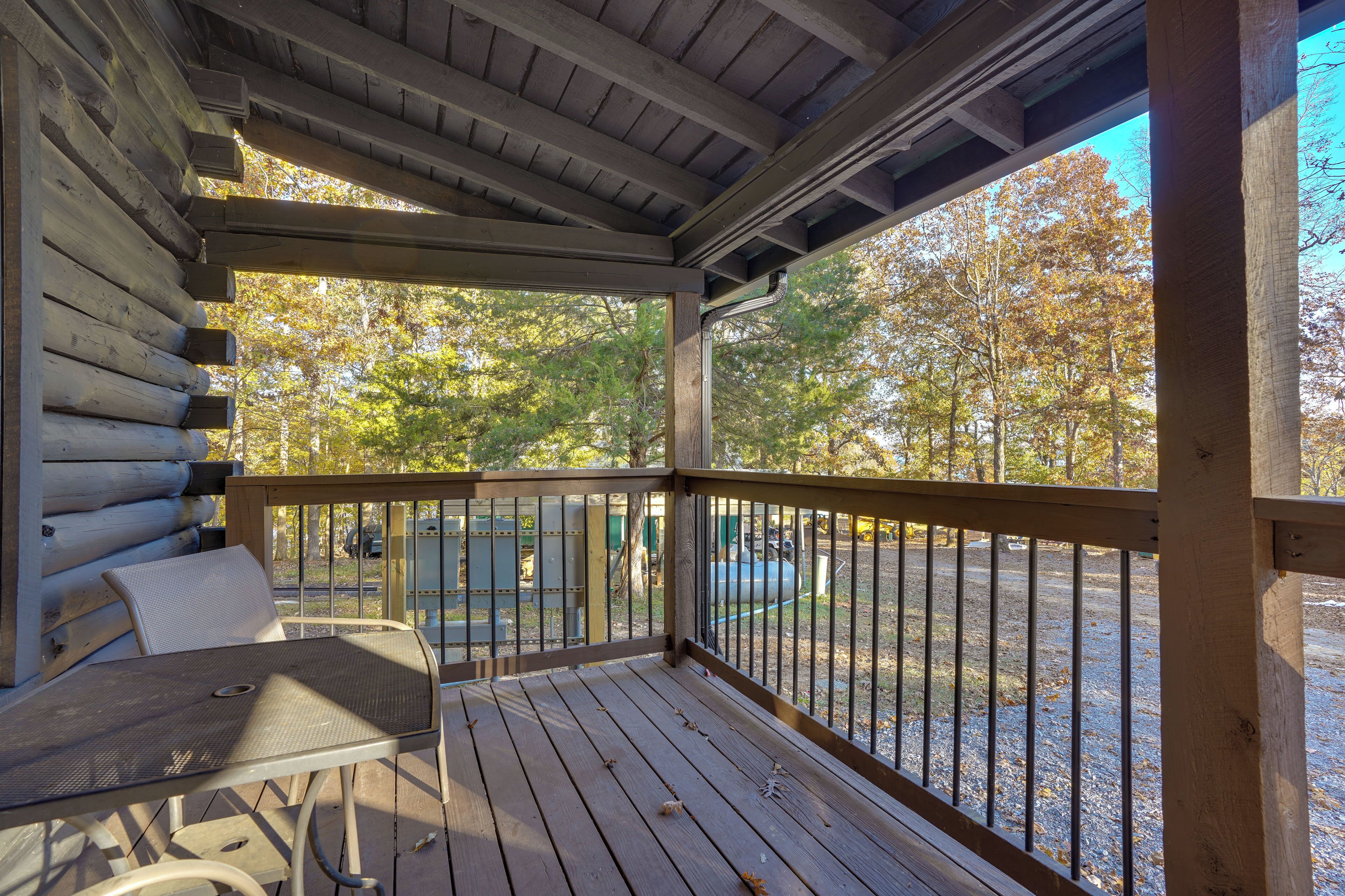 A wooden deck with a table and chairs, overlooking a parking area and trees.