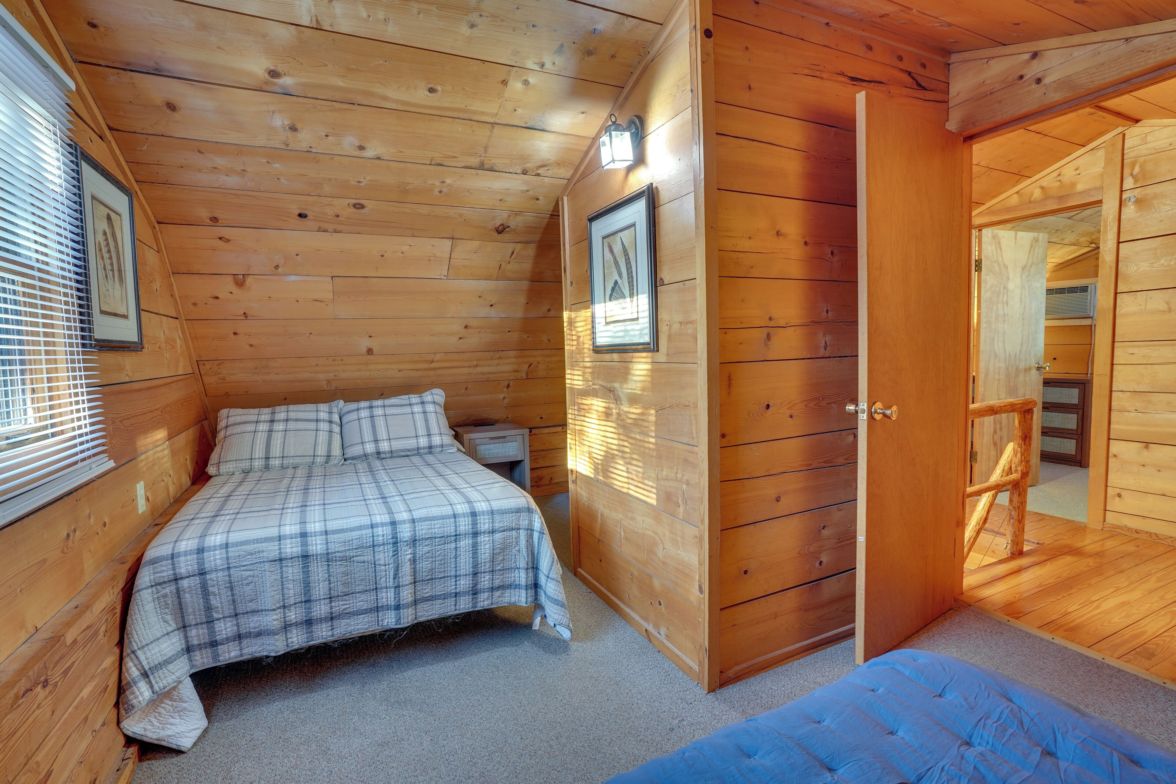 A wooden cabin bedroom with a bed, a dresser, and a door leading to another room.