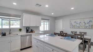 A modern kitchen with white cabinetry, a central island, and a dining area with wooden chairs. - 6 Mi to Saguaro Natl Park! Family Home w/ Patio (Tucson)