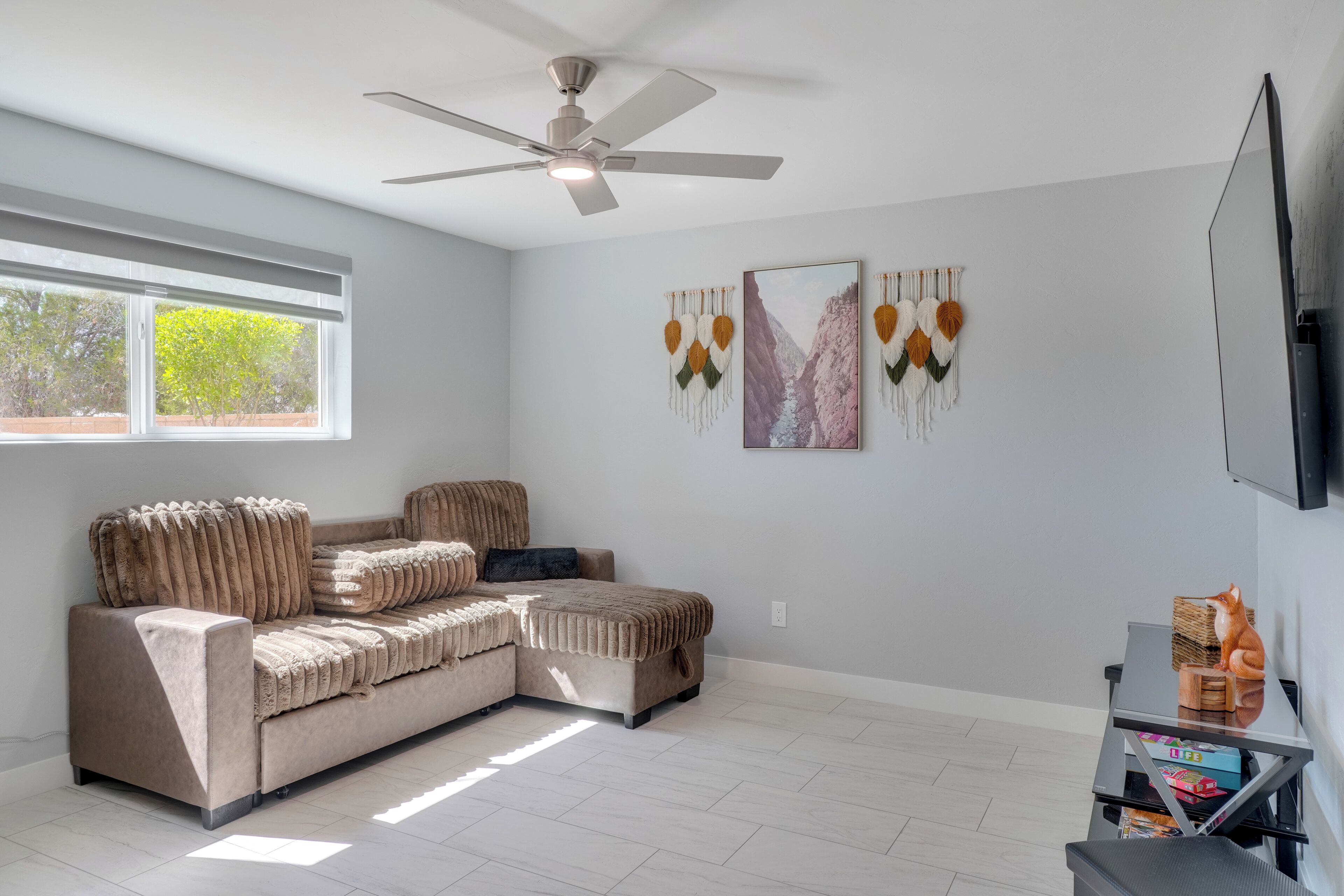 A modern living room with a sectional sofa, a ceiling fan, a flat-screen TV, and wall art.