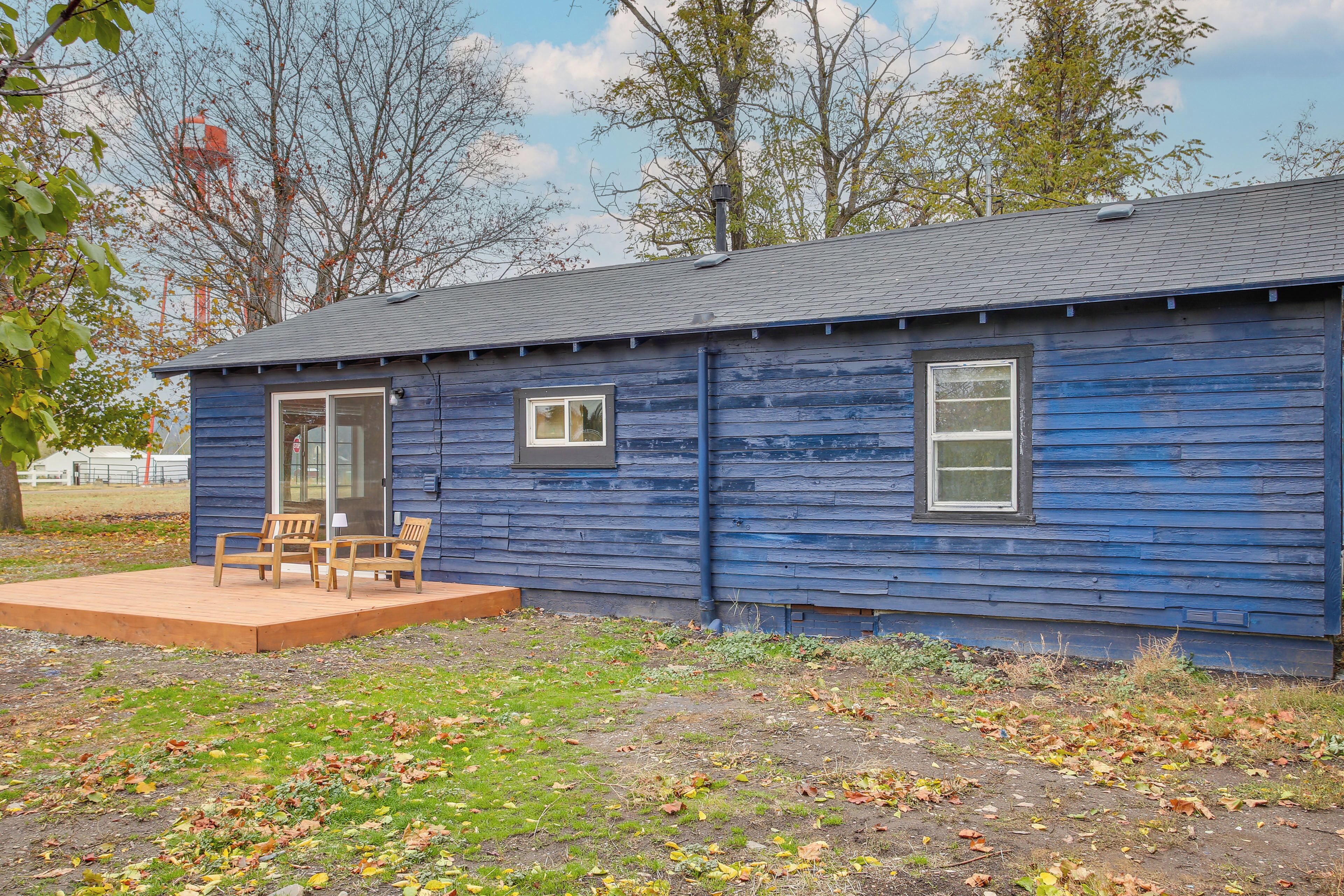 A small, single-story house with a blue exterior, a front porch with wooden chairs, and a small window.