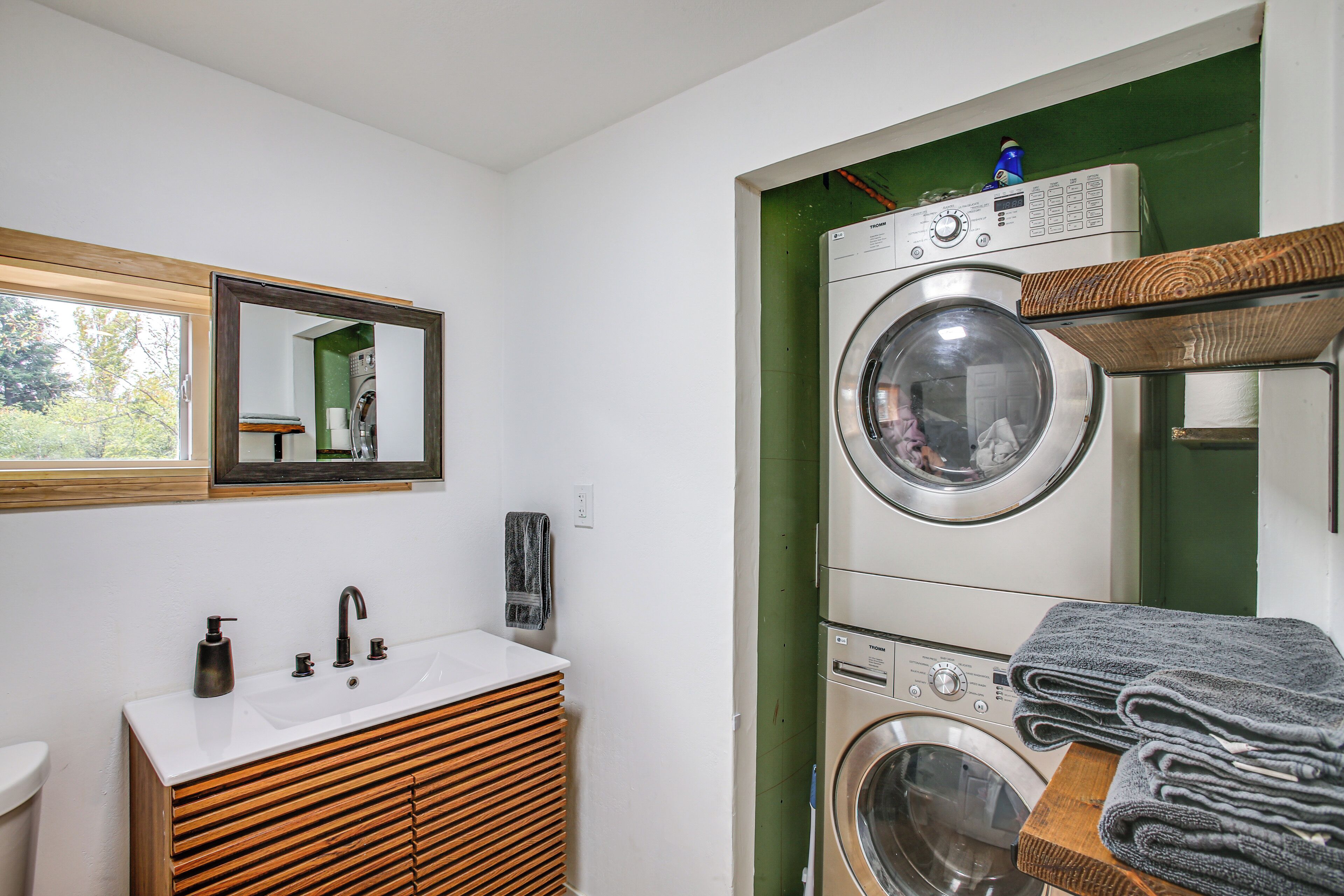 A compact laundry room with a washing machine, dryer, and a sink with a wooden vanity.