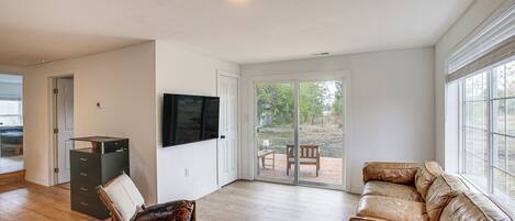 Un salón amplio con un sofá de cuero, una silla de madera, un televisor y un ventanal corredero que da a un patio exterior.