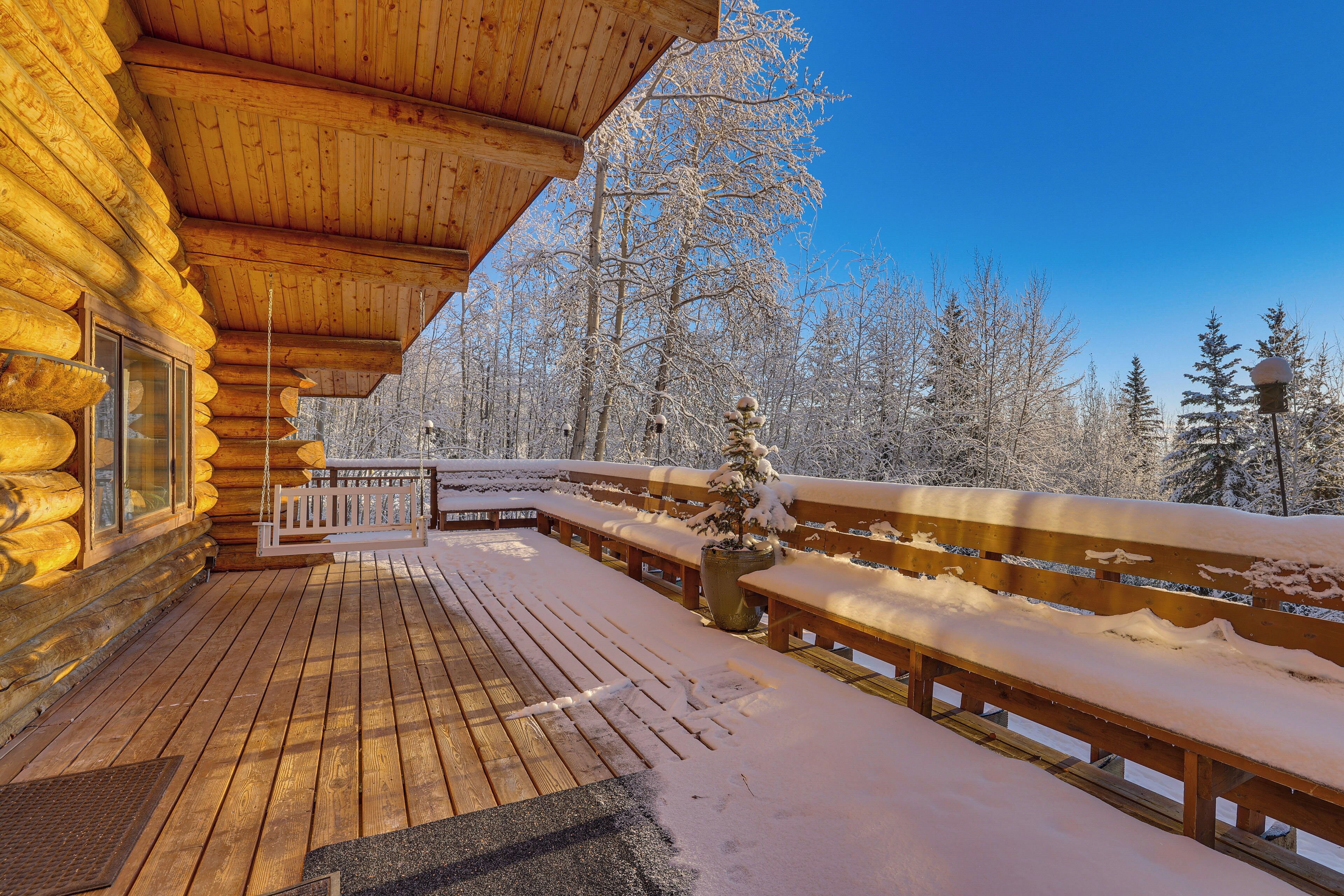 A wooden deck with benches and a wooden railing, surrounded by snow-covered trees.