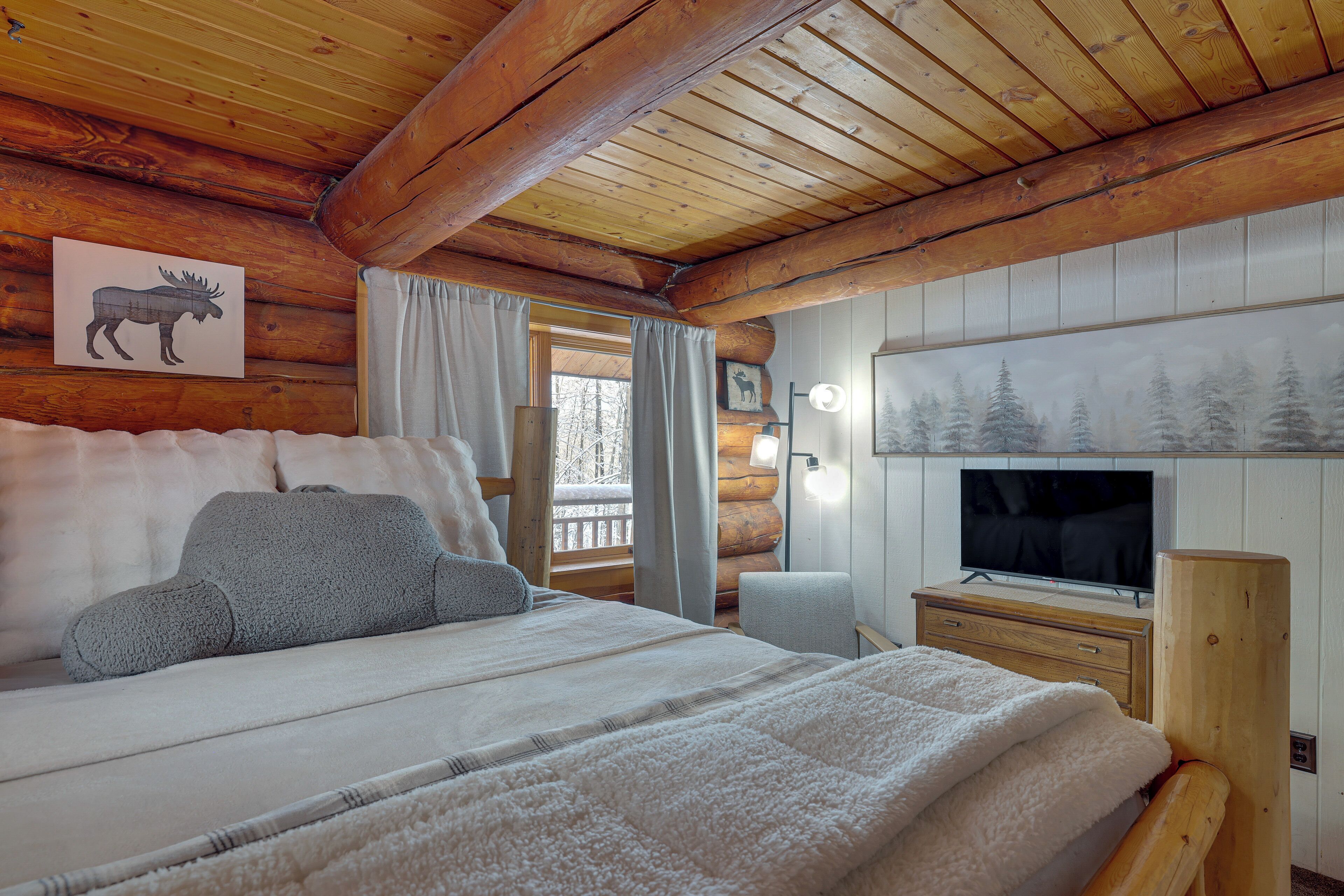 A cozy log cabin bedroom with a large bed, a television, and a window with curtains.
