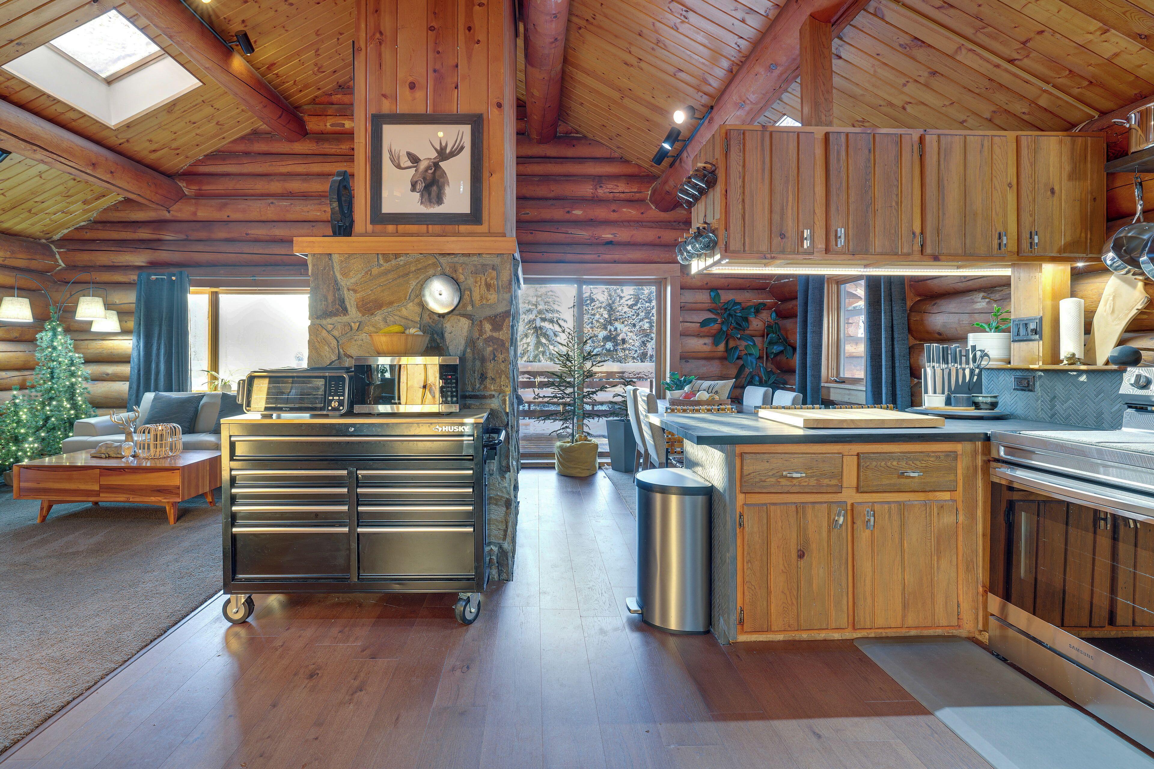 A log cabin interior with a kitchen, dining area, and a visible Christmas tree.