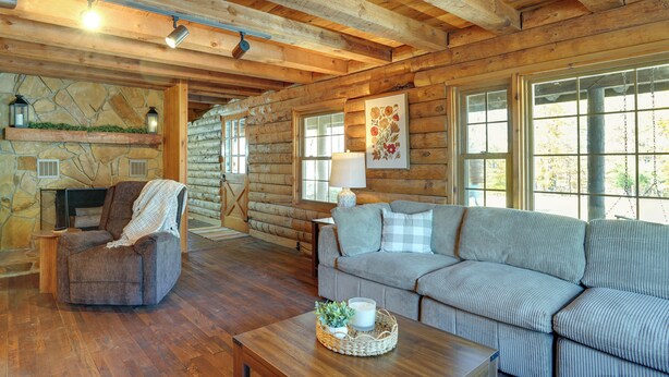 L’intérieur d’une cabane en rondins, avec une cheminée en pierre, un canapé, un fauteuil et une table basse en bois.
