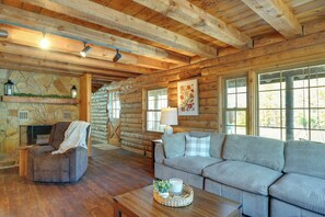 L’intérieur d’une cabane en rondins, avec une cheminée en pierre, un canapé, un fauteuil et une table basse en bois.