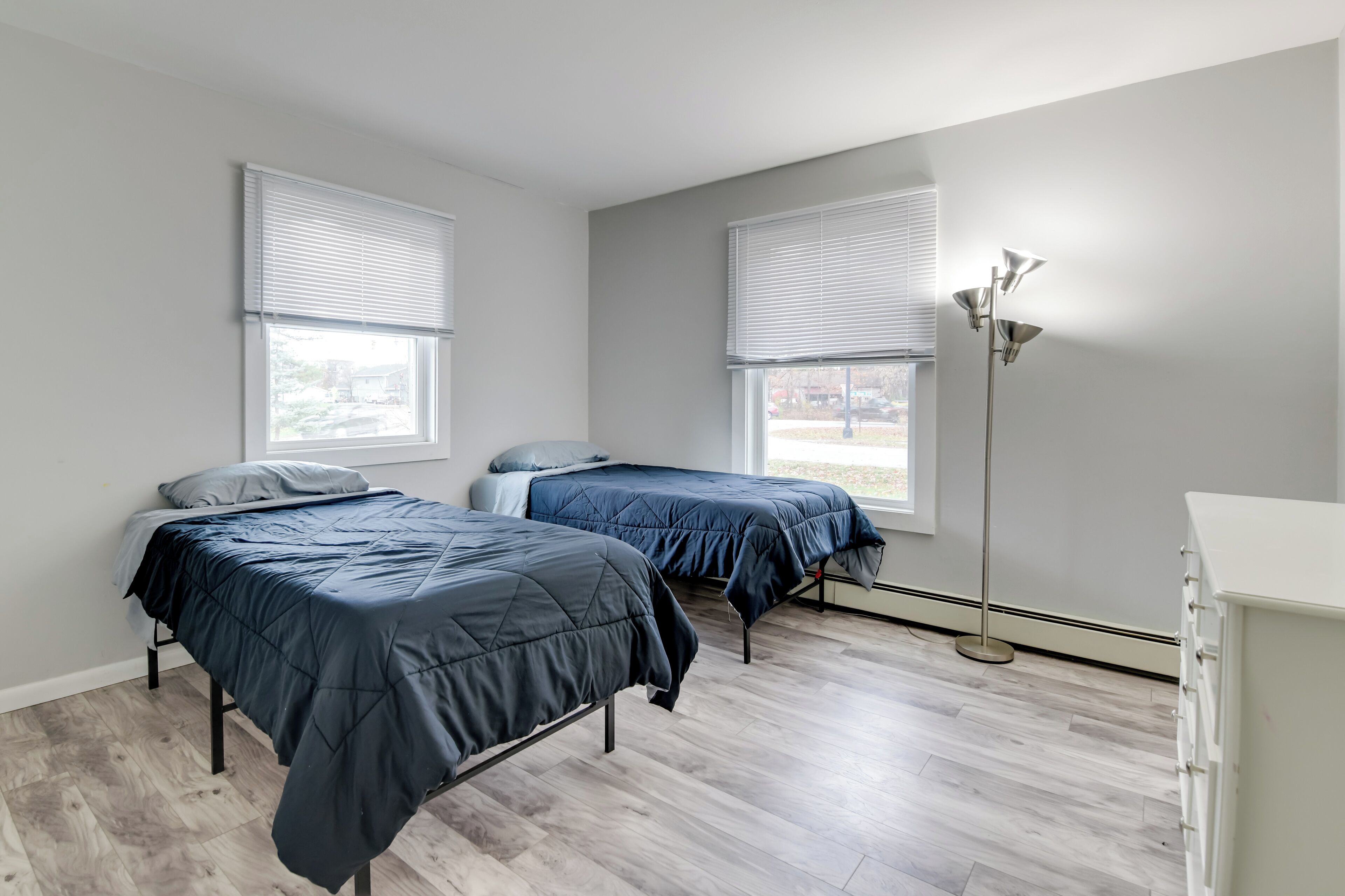 A bedroom with two beds, a floor lamp, and a dresser.