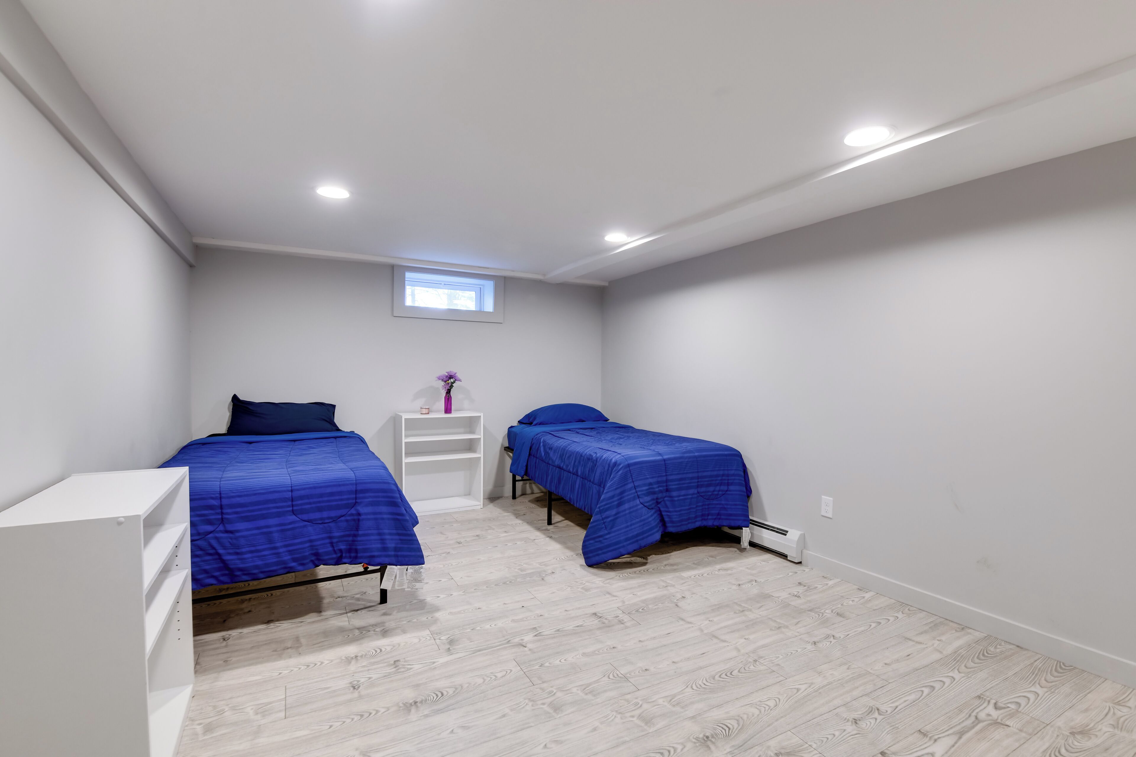 A bedroom with two beds, a small window, and a white wardrobe.