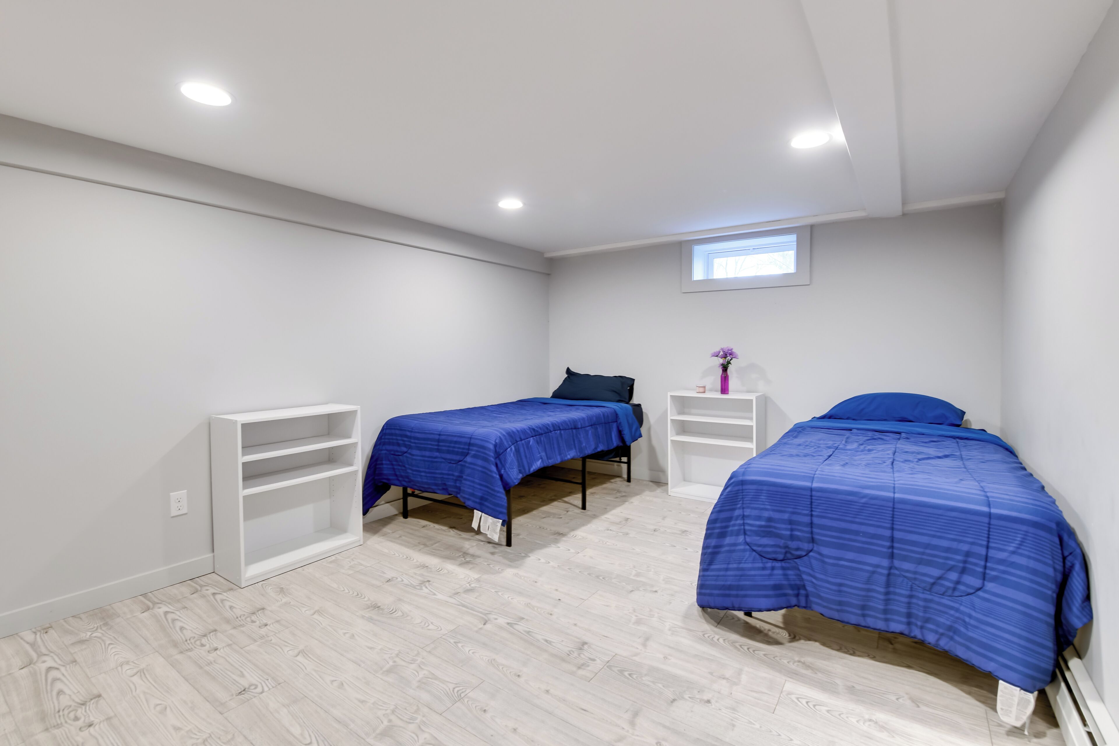 A bedroom with two beds, white shelving units, and a small window.