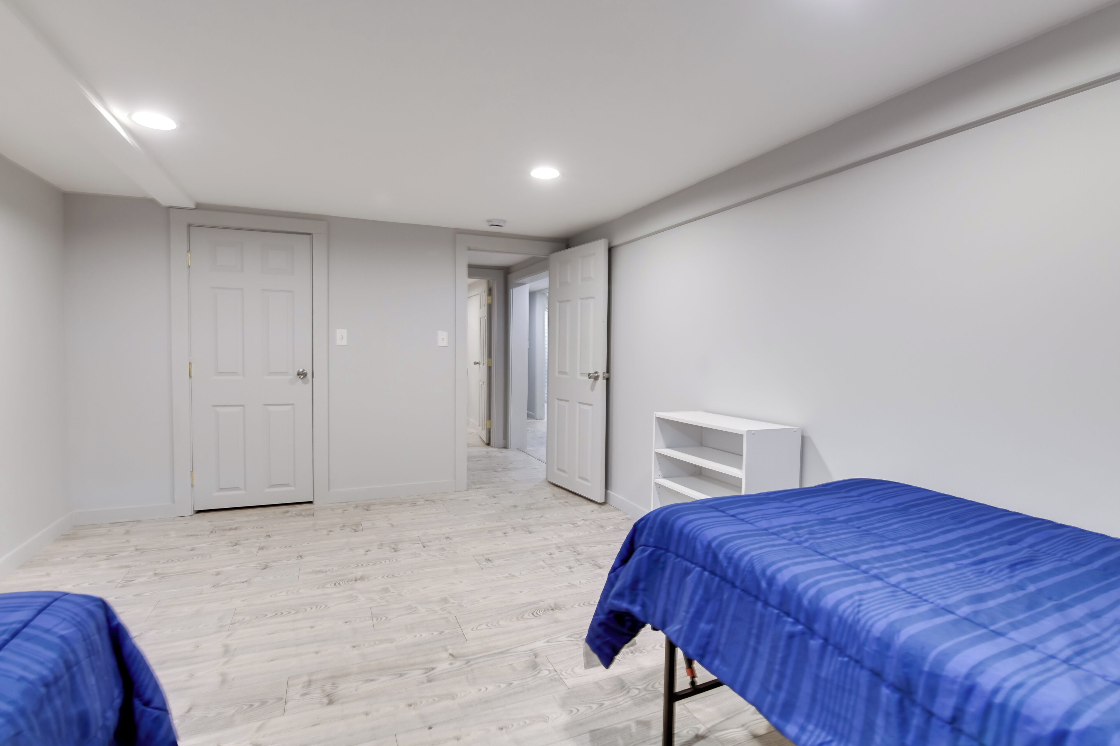 A room with two beds, white walls, and a wooden floor.