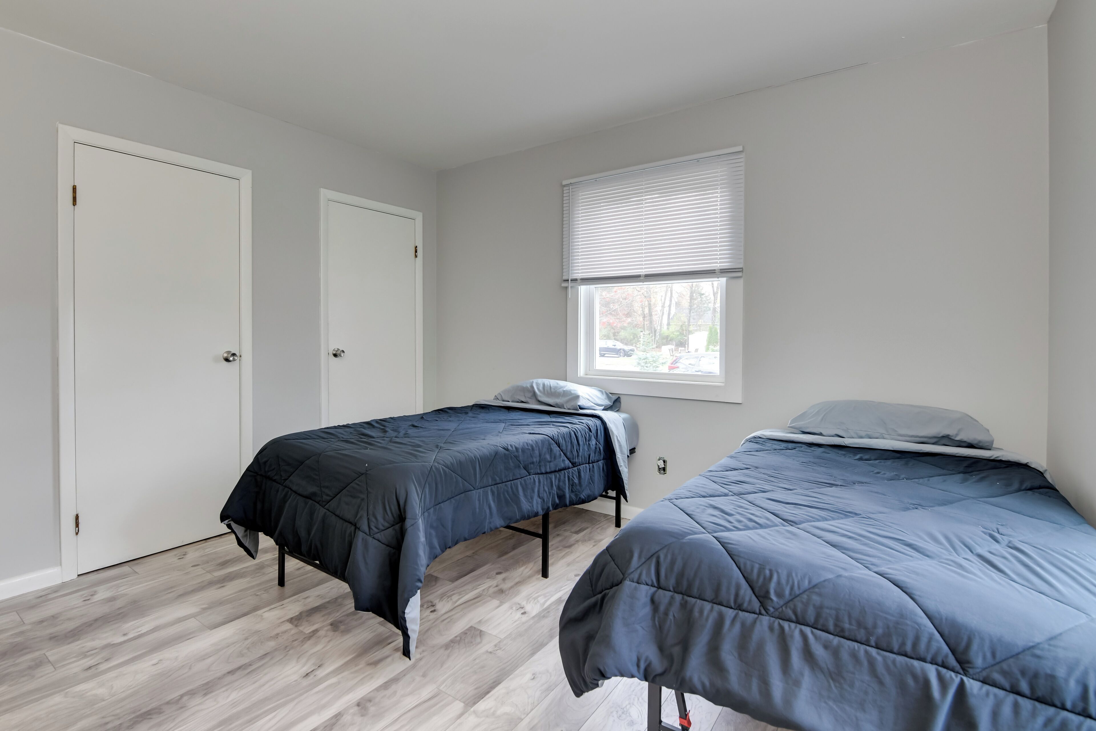 Une chambre avec deux lits simples, une fenêtre avec des stores et une porte.