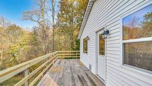 A wooden deck with a railing, a white building with large windows, and a forested background. - Dirt Road Digs - Quiet Home in Lakeville! (Lakeville)