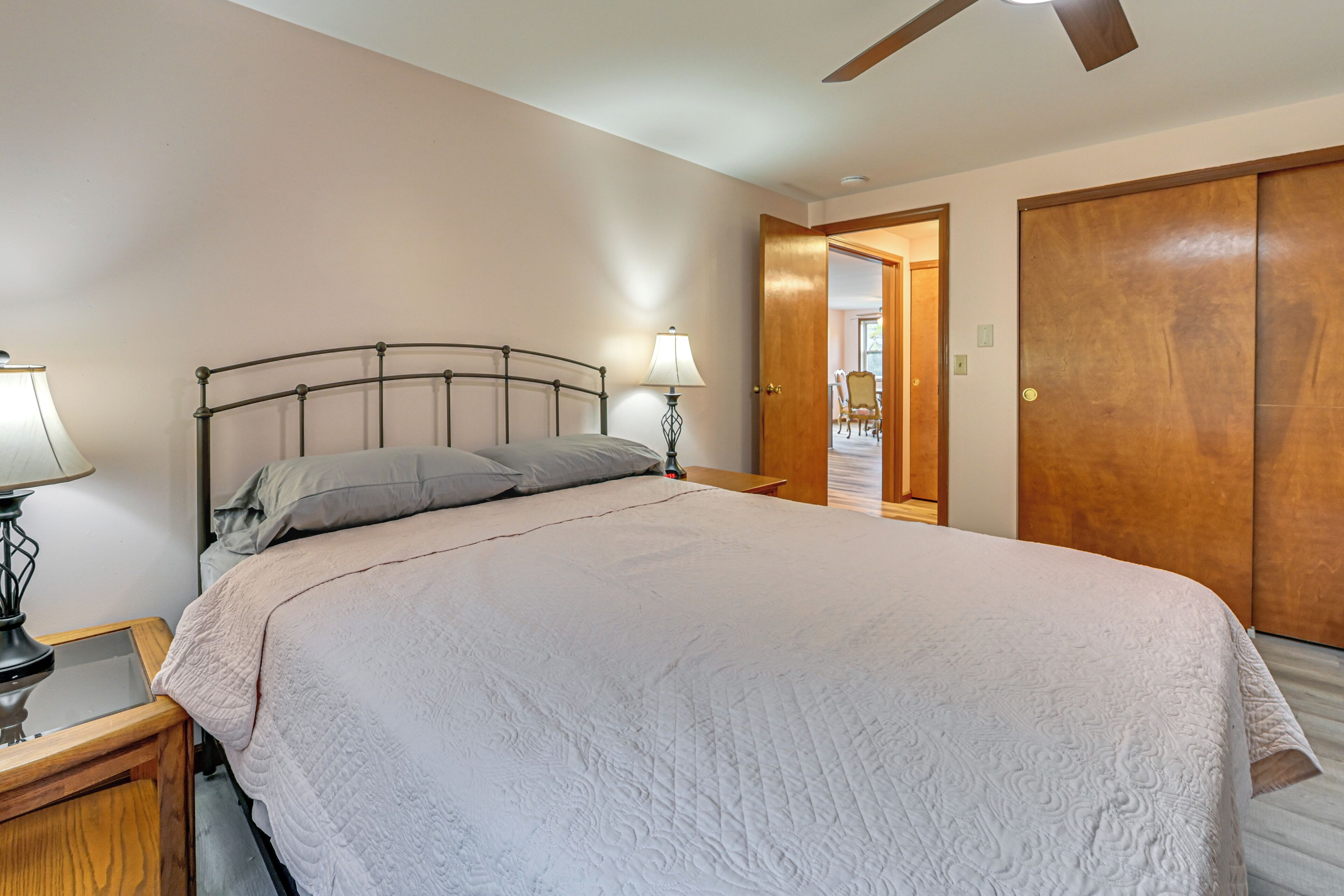 Une chambre à coucher avec un lit, une table de chevet avec une lampe, une porte en bois et un ventilateur de plafond.