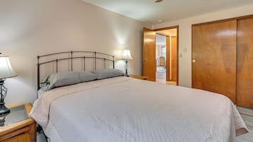 Un dormitorio con cama, una mesita de noche con lámpara, una puerta de madera y un ventilador de techo.