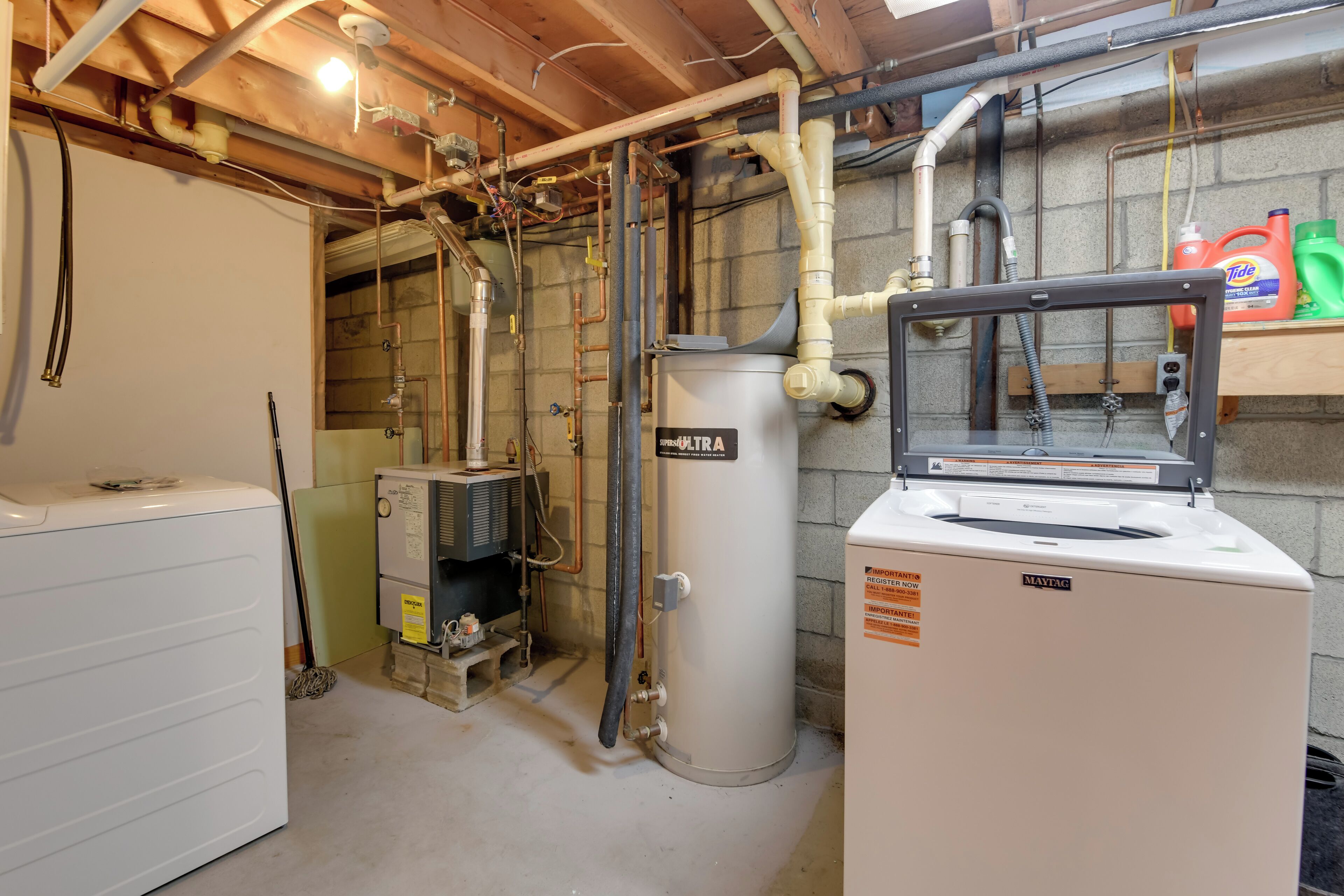A utility room with a water heater, a washing machine, and various pipes and ducts.
