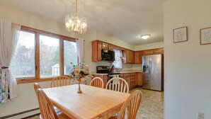 A kitchen with wooden cabinets, stainless steel appliances, and a dining area with a wooden table and chairs. - 15 Mi to Cochran's Ski Area: Cozy Home w/ Yard! (Essex Junction)