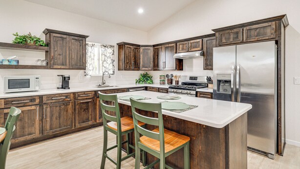 A modern kitchen with wooden cabinets, a stainless steel refrigerator, and a central island with chairs. - Hike & Ski! Home w/ Dog-friendly Yard in Eagar (Eagar)